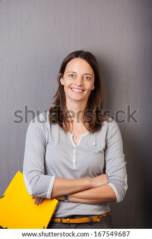 Attractive confident woman standing with folded arms holding a bright yellow folder while smiling at the camera