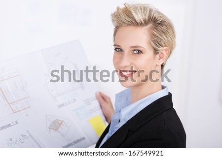 Smiling successful businesswoman working at her desk turning to look at the camera with a view down to the blurred notes on her desk