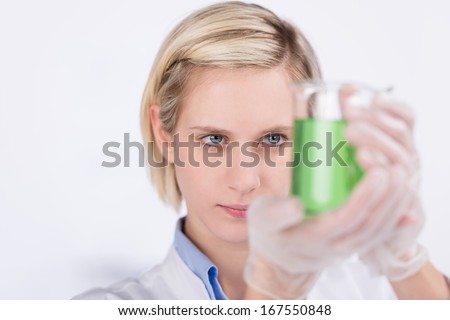 Young woman in a lab examining a chemical solution in a glass beaker as she conducts quality control tests, diagnostic tests or experiments