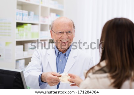 Helpful elderly male pharmacist dispensing medicine to a female patient with a friendly sympathetic smile