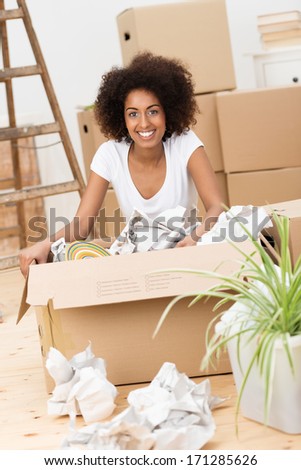 Beautiful African American woman packing to move house sitting on the hardwood floor in front of a brown cardboard carton surrounded by crumpled paper