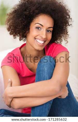Smiling African American woman with an Afro hairstyle sitting hugging her knee and beaming at the camera