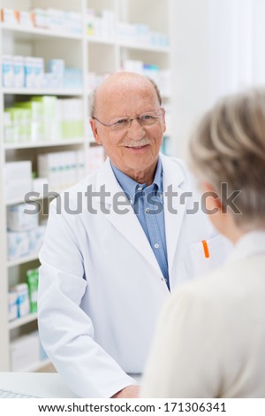 Sympathetic friendly male pharmacist standing at the counter in the pharmacy talking to a female patient listening to her problems with a gentle smile