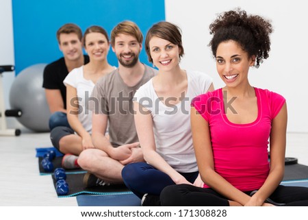 Group of young friends practicing yoga at the gym sitting cross legged on the floor in the lotus position smiling happily at the camera