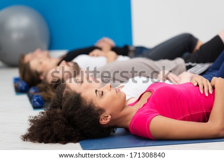 Aerobics class practicing deep breathing for relaxation lying on their backs on their mats on the floor with focus to a young African American woman in the foreground