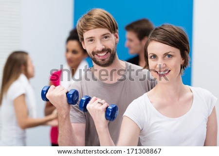 Attractive happy smiling young couple working out at the gym with dumbbells to strengthen and tone their muscles, close-up head and shoulders