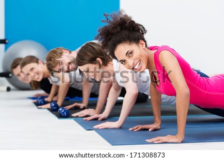 Group of fit young people doing push ups while working out in a class in the gym with focus to a beautiful vivacious young African American woman in the foreground