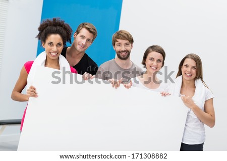 Fitness group of diverse sporty young people at the gym holding up a large blank white card with copyspace for your text or advert