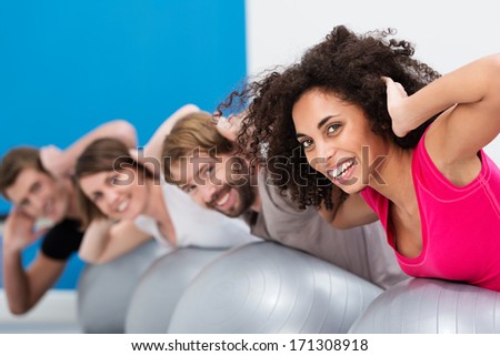 African American Woman In Pilates Class At The Gym With A Group Of Her Friends Turning To Smile Happily At The Camera During Their Workout