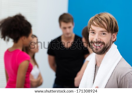Attractive young bearded man with a beaming friendly smile posing in front of a group of his his friends at the gym