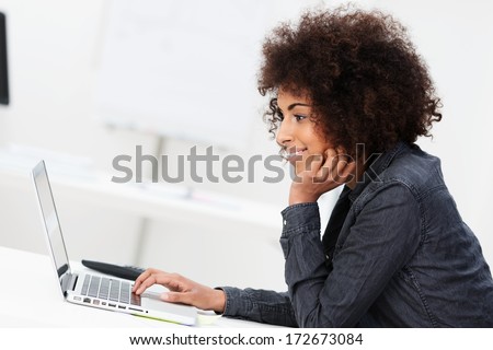 Side view of a young African American businesswoman with an afro hairstyle using a laptop computer sitting concentrating on information on the screen