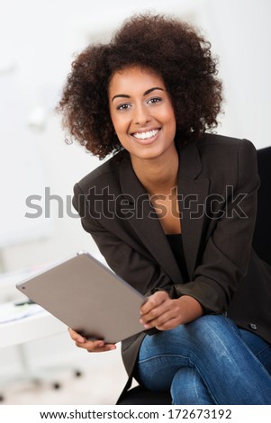 Friendly African American businesswoman with a beautiful smile and afro hairstyle sitting holding a tablet computer looking at the camera