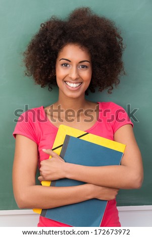 Beautiful young African American student clasping her files containing class notes to her chest as she stands smiling at the camera