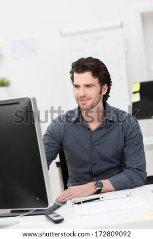 Handsome Young Businessman Working At His Desktop Computer Sitting At His Desk In The Office