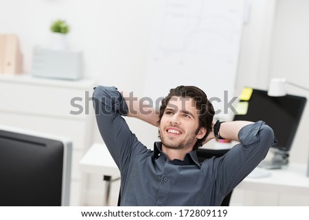 Successful businessman relaxing in his chair leaning back with his hands behind his head looking into the air smiling