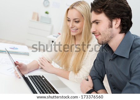 To co-workers in the office working on a laptop computer with a beautiful young woman smiling as she presents something to her male colleague