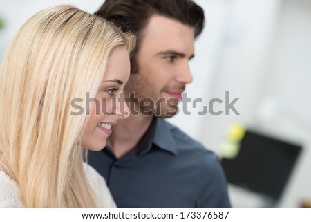 Attractive young couple standing side by side looking to the right of the frame with focus to the beautiful blond woman