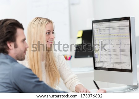 Female and male office co-workers sitting on a desk in front of a computer monitor working together