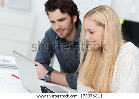 Business Team Consisting Of A Young Man And Woman Sitting Working Together At A Laptop And Smiling As They Access Information On The Screen