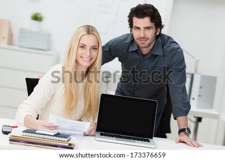 Young businessman and woman in the office sitting at a desk with their laptop screen turned to face the camera with copyspace for your text or advertisement