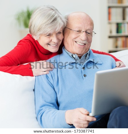 Amused Senior Couple Using A Laptop Computer Laughing As They Look At Something On The Screen With The Wife Leaning Over Her Husbands Shoulder For A Better Look