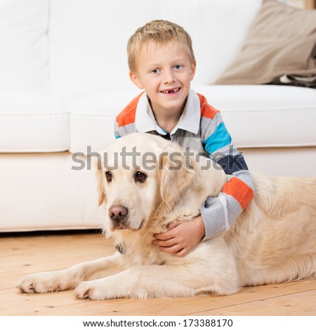 Smiling little boy missing his front teeth bending down playing with a golden retriever on the living room floor and grinning at the camera