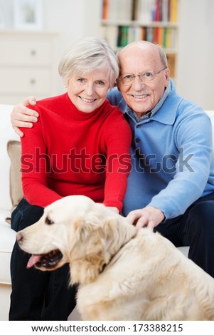 Loving elderly couple embracing each other sitting on the sofa with their golden retriever dog in front of them