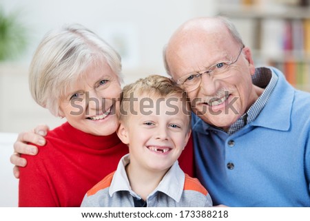 Beautiful Family Portrait Showing The Generations With A Cute Little Boy With His Front Teeth Missing Sitting With His Happy Smiling Grandparents In A Close Embrace