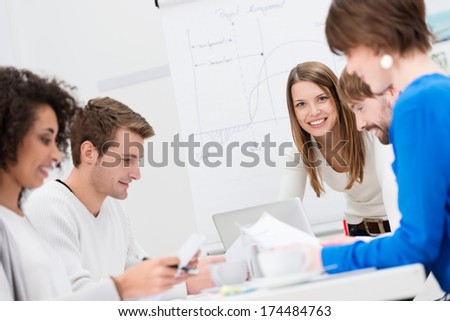 Female team leader with her business team conducting a brainstorming and strategy planning meeting as they sit around a table in the office, focus to her smiling face