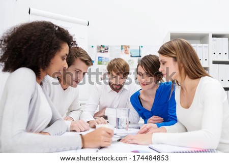 Dedicated young multiethnic business team in a meeting sitting grouped around a table in the office holding a serious discussion as they analyze paperwork