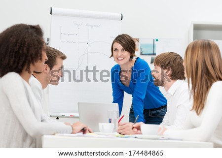 Businesswoman Giving A Presentation To Her Team As She Stands In Front Of A Flip Chart And Laptop Computer Smiling As She Answers Questions
