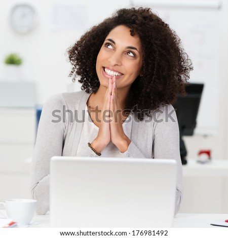 Beautiful vivacious smiling African American businesswoman offering a prayer of thanks at her desk for a successful business outcome
