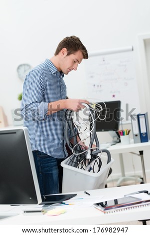Businessman putting a jumbled mess of computer cables in a bin as he switches his office to wireless technology