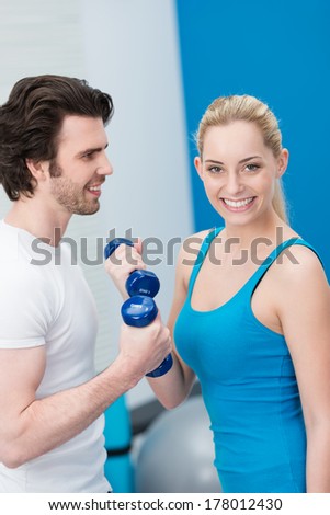 Beautiful young woman working out in a gym with dumbbells together with a handsome young male friend as they tone and strengthen their arm muscles