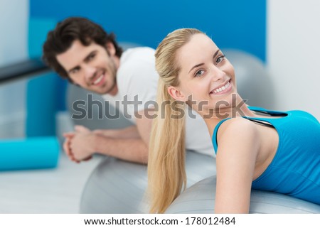 Beautiful blond woman with a lovely friendly smile working out in a gym with a male friend using Pilates gym balls