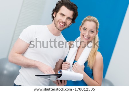 Beautiful young woman with her handsome male gym instructor or personal fitness trainer at the gym