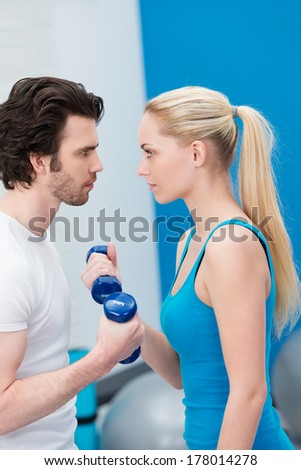 Intense young couple working out with dumbbells standing face to face exercising together and egging each other on to greater achievements