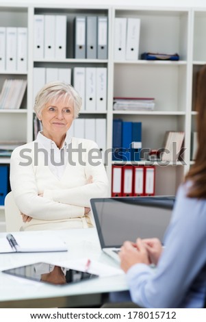 Senior woman attending a meeting in an office sitting back with a smile as she listens to her female business adviser