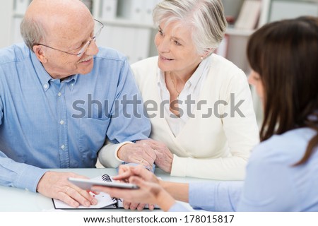 Affectionate elderly couple in a business meeting holding hands as they discuss a proposal put forward by their broker