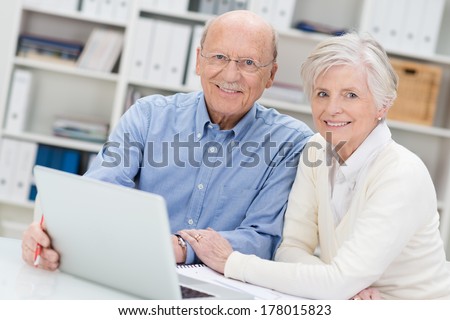 Senior couple working on a laptop in an office sitting close together as they share the screen and catch up on social media contacts