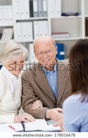 Broker chatting to a smiling senior couple as they sit at the desk in her office discussing finances or insurance