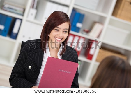 Smiling young Asian woman in a job interview sitting talking to the employment officer with her curriculum vitae in her hands