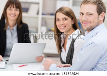 Attractive smiling couple talking to an agent or investment adviser sitting at a desk in her office turning to smile at the camera