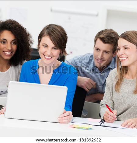 Smiling diverse multiethnic business team grouped around a laptop as they share their thoughts and ideas