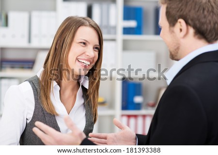 Happy laughing young businesswoman sharing a joke with a male colleague as they take a break in the office