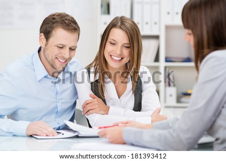 Investment adviser giving a presentation to a friendly smiling young couple seated at her desk in the office