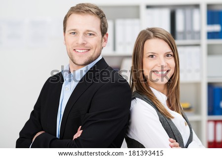 Attractive successful business partners with a young man and woman posing back to back with folded arms smiling confidently at the camera