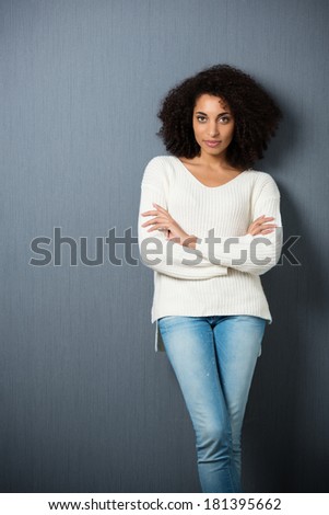 Beautiful serious African American woman leaning against a dark background with crossed legs and folded arms looking at the camera with copyspace and vignetting