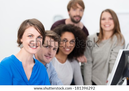 Confident multiethnic young business team lead by a smiling attractive young women working together in the office at a desktop computer