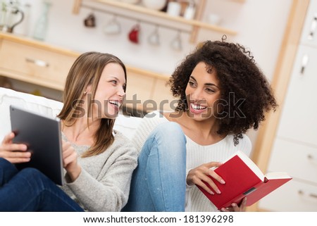 Two female friends enjoying as relaxing day together laughing and having fun as they read a book and e-book